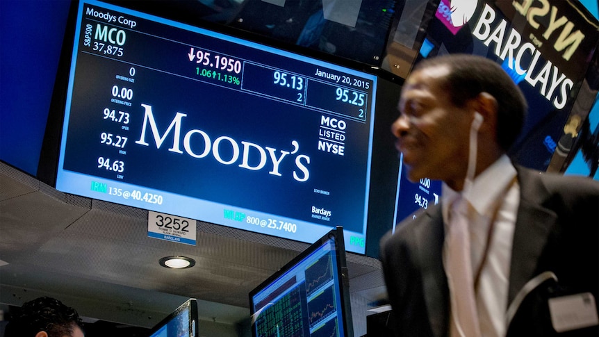 A screen displays Moody's ticker information as traders work on the floor of the New York Stock Exchange.