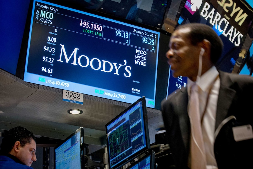 A screen displays Moody's ticker information as traders work on the floor of the New York Stock Exchange.