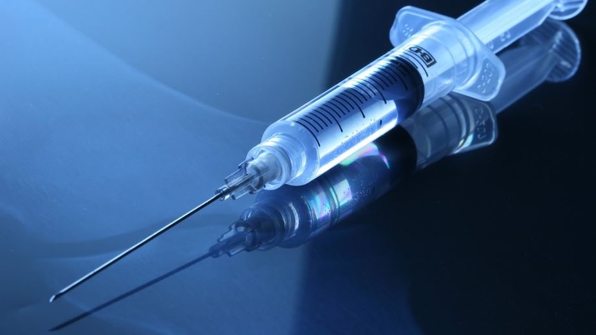 Picture of a syringe on a dark reflective surface 
