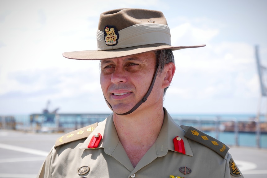 A man in an Australian Army uniform and hat stands on the deck of a ship