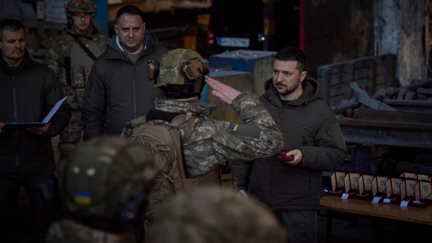 A soldier in uniform salutes a civilian politician in a dark room.