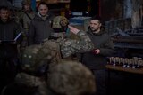 A soldier in uniform salutes a civilian politician in a dark room.