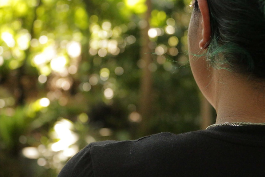 A woman stands in a park with only her ear and shoulder visible.