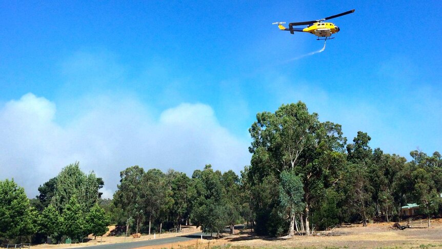 A water-bombing helicopter banks away after dumping its load of water on a bushfire at Parkerville.