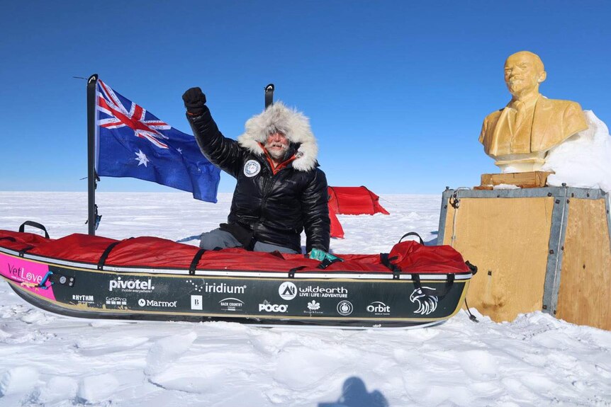 A man and a snow sled next to a statue in Antarctica