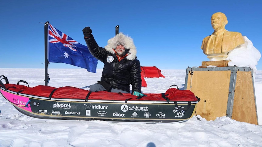 A man and a snow sled next to a statue in Antarctica