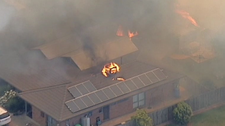 An air conditioning unit on fire on top of a house in a bushfire.