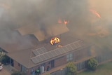 An air conditioning unit on fire on top of a house in a bushfire.