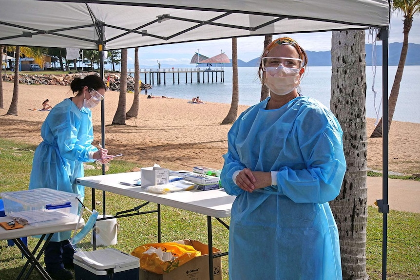 Two nurses in protective coverings and face masks work inside a temporary tent erected on the foreshore of Townsville's Strand