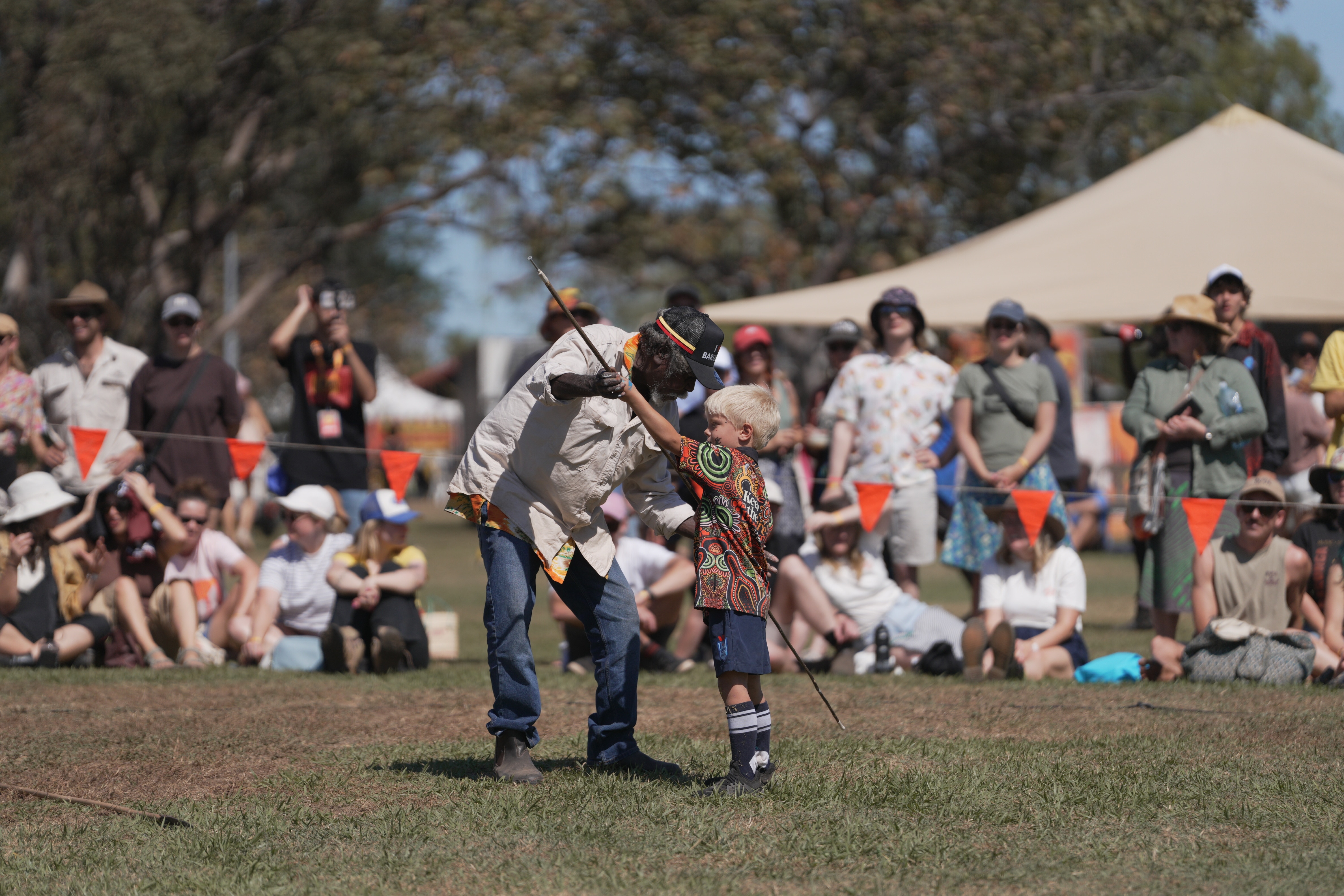 A man shows a small boy how to throw a spear.