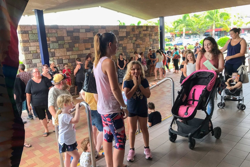 A line of people snakes out the door. Mostly mothers and children in the queue. A little girl holds her face with anticipation.