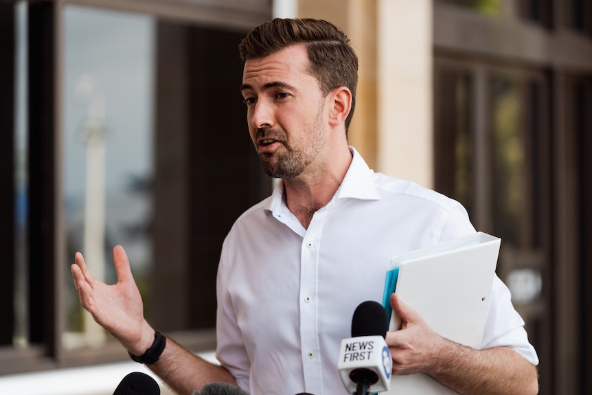A mid-shot of WA Opposition Leader Zak Kirkup wearing a white business shirt, holding a white folder and talking to reporters.