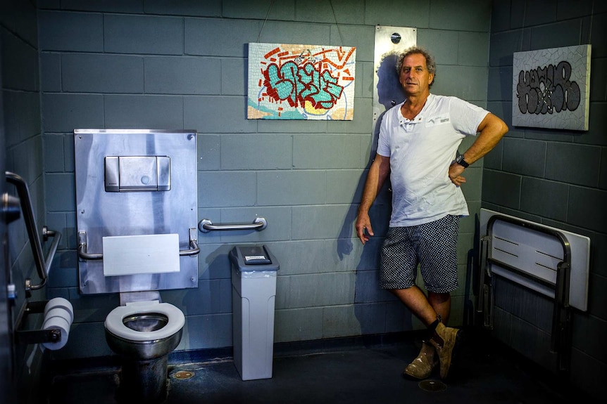 Male artist stands in toilet with mosaic work
