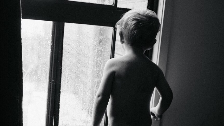 A small boy stands at a window