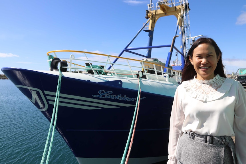 Large boat tied up at wharf with woman in foreground on the right looking at camera