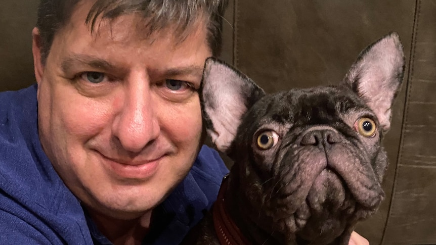 A middle-aged man holding a French bulldog.