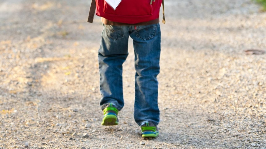 A close-up of a child walking with a backpack, showing only their legs and the bottom of the bag.