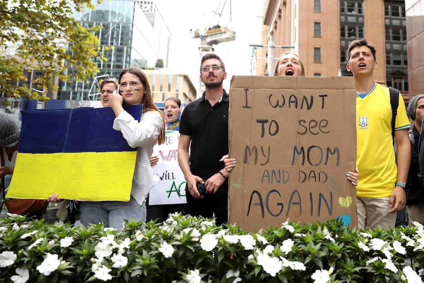 Protesters in Sydney hold a sign of the Ukrainian flag and one that reads "I want to see my mom and dad again".