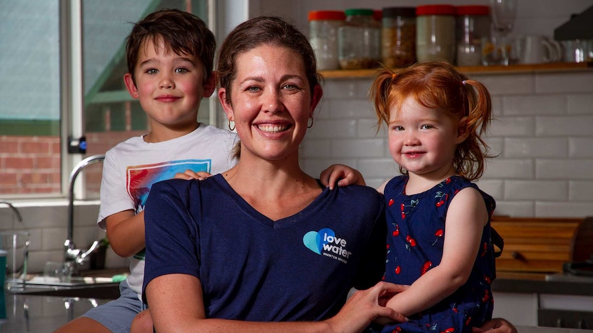 A woman wearing a blue T-shirt in a kitchen with a boy aged four and a girl aged 2.