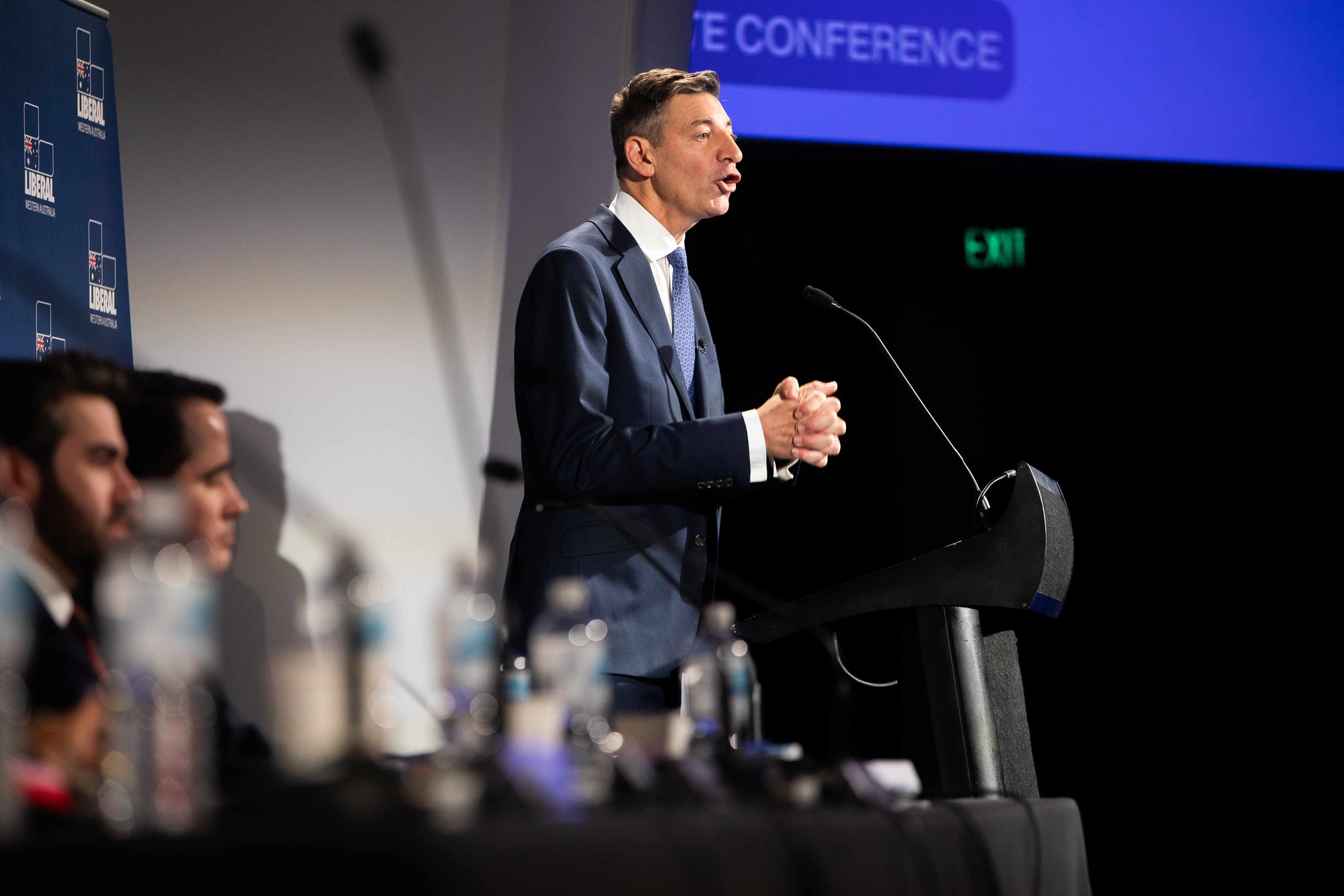 Basil Zempilas grips his hands together while speaking at a lectern.