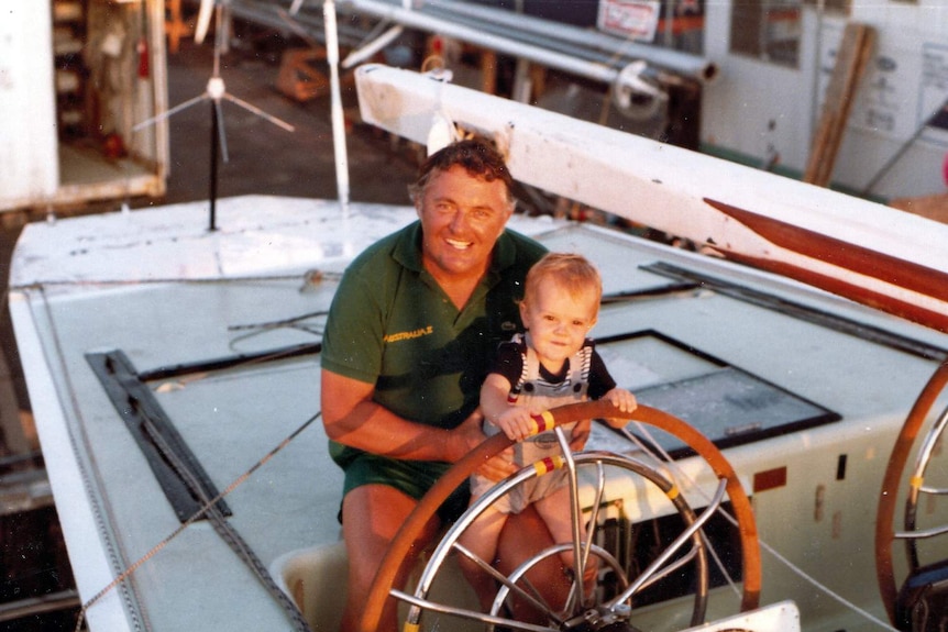 Alan Bond sits at the wheel of Australia II with a child, Jeremy, in 1983.