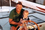 Alan Bond sits at the wheel of Australia II with a child, Jeremy, in 1983.