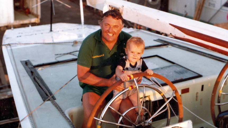 Alan Bond sits at the wheel of Australia II with a child, Jeremy, in 1983.