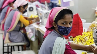Female Bangladeshi garment maker sewing clothes and wearing a face mask.