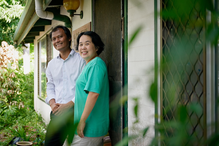 A man and a woman standing outside the door of a house, smiling and looking at the camera. 