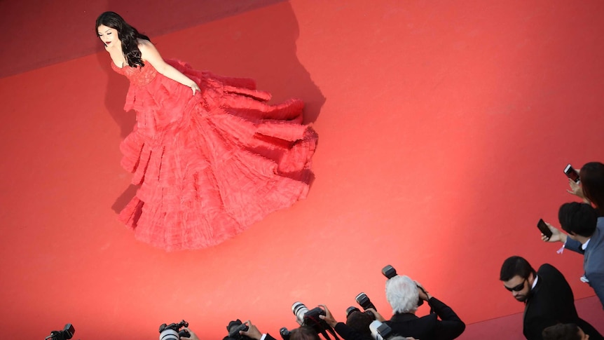 A woman in a red dress poses for photographers on the red carpet.