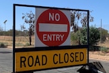 "Road closed", "no entry" sign on a street in front of a fenced community.