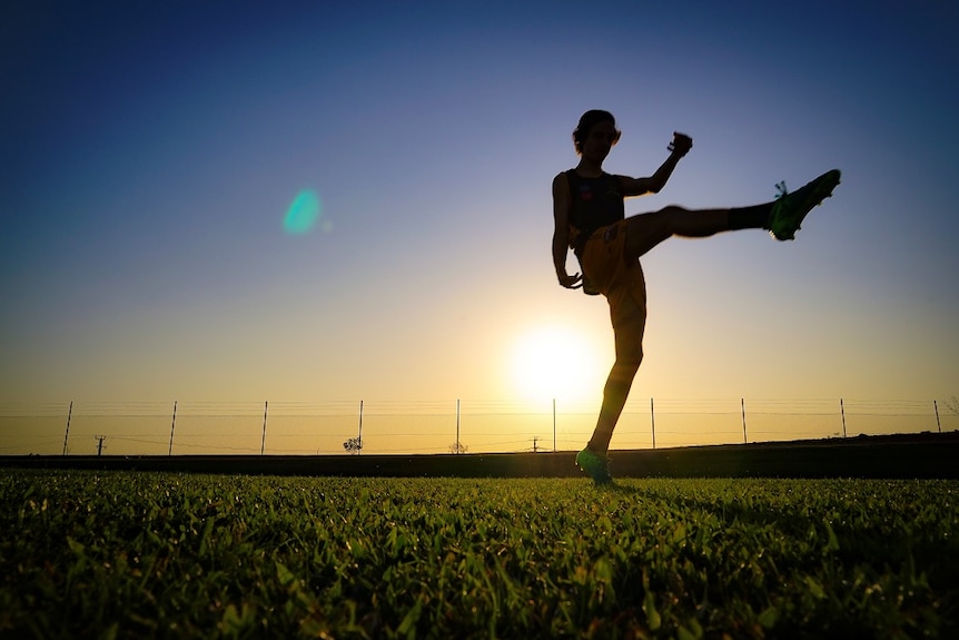 Jacob Long is pictured kicking a football, as the sun sets behind him