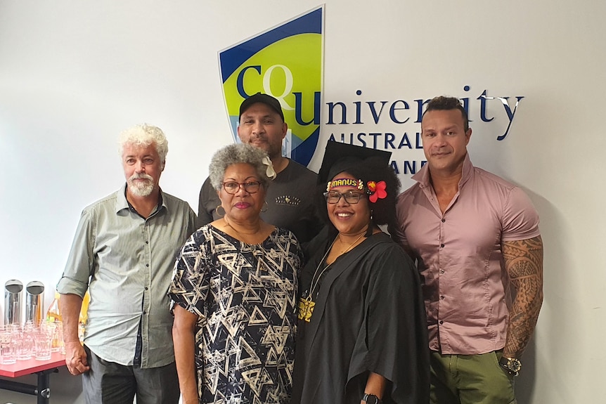 Sophie standing among members of her family in front of a CQ University sign. 