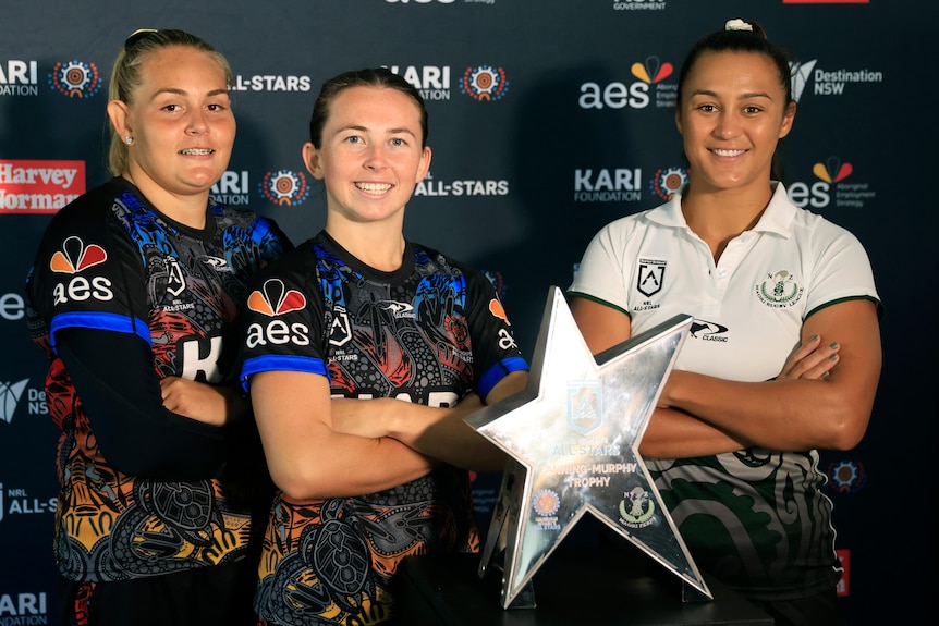 Caitlan Johnston, Quincy Dodd and Corban Baxter stand smiling, arms folded, with a star shaped trophy in the foreground