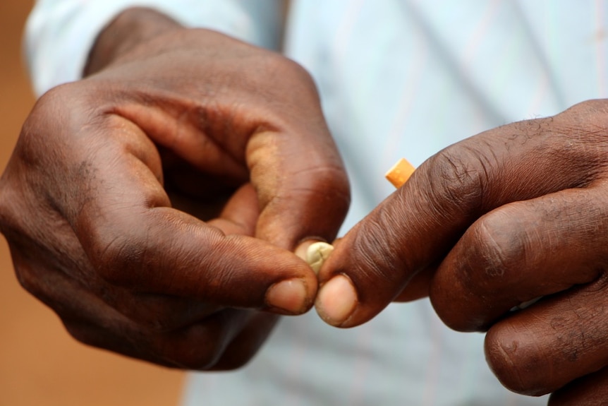 A man peeling a coffee bean with a cigarette in his hand