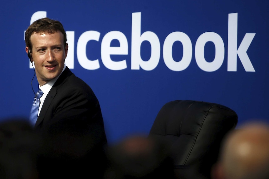 Mark Zuckerberg in front of a Facebook sign