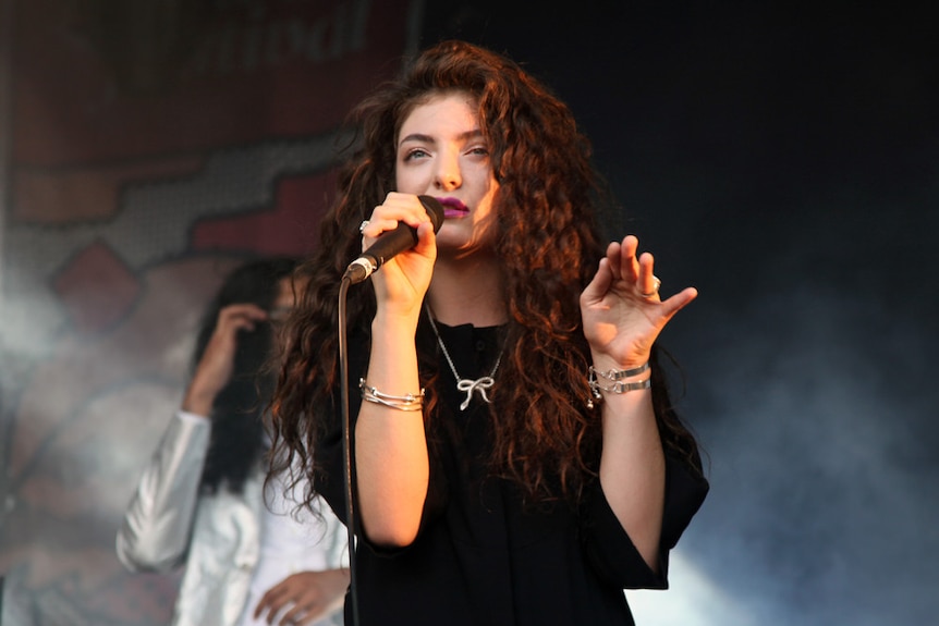 Lorde raises one hand while singing at the Laneway Festival.