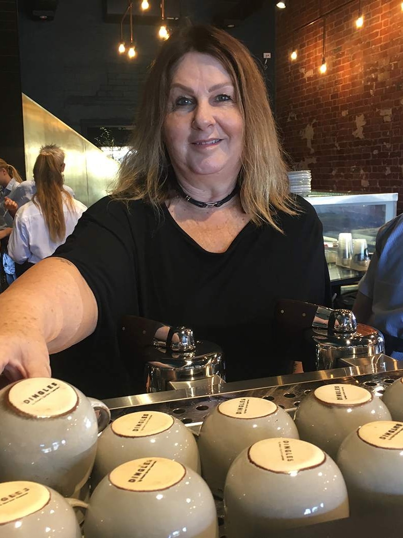 Woman stands behind a stack of coffee mugs at a cafe in Rockhampton with workers in background