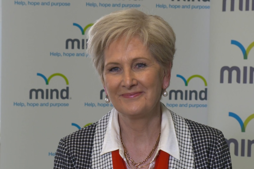 A blond woman in checked top smiling with mind australia logo banner in the background. Ausnew Home Care, NDIS registered provider, My Aged Care