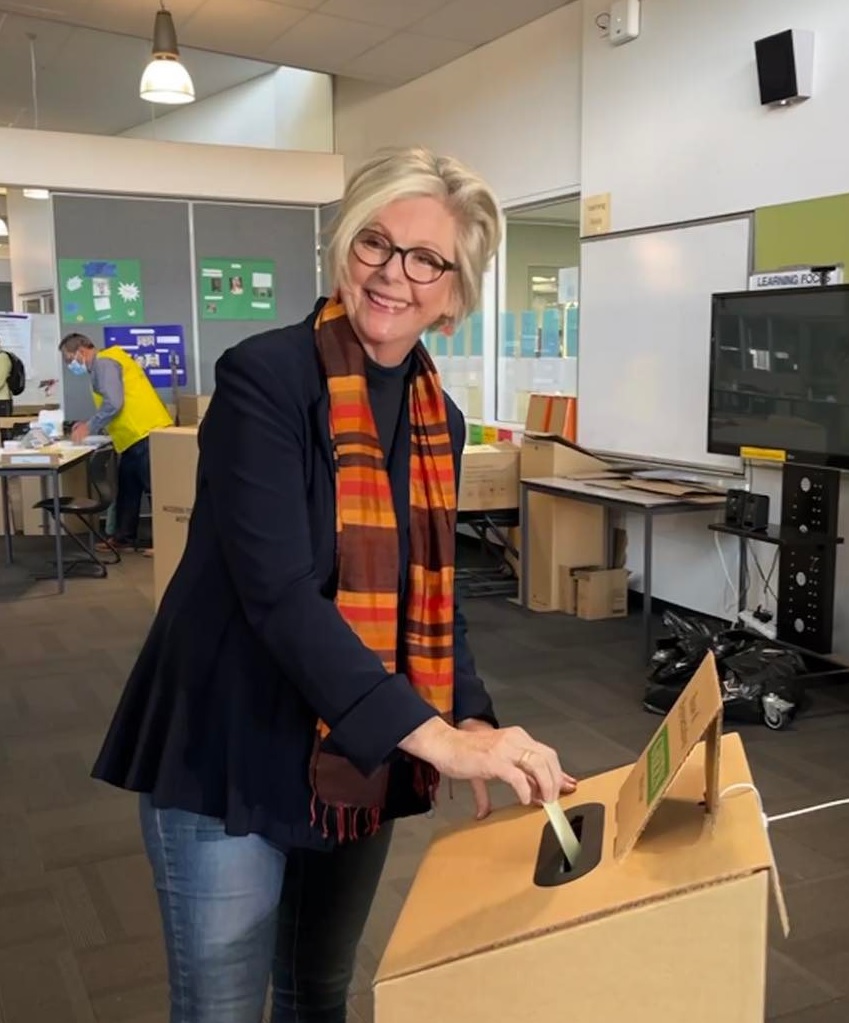 women with an organgy scarf placing her vote in the box