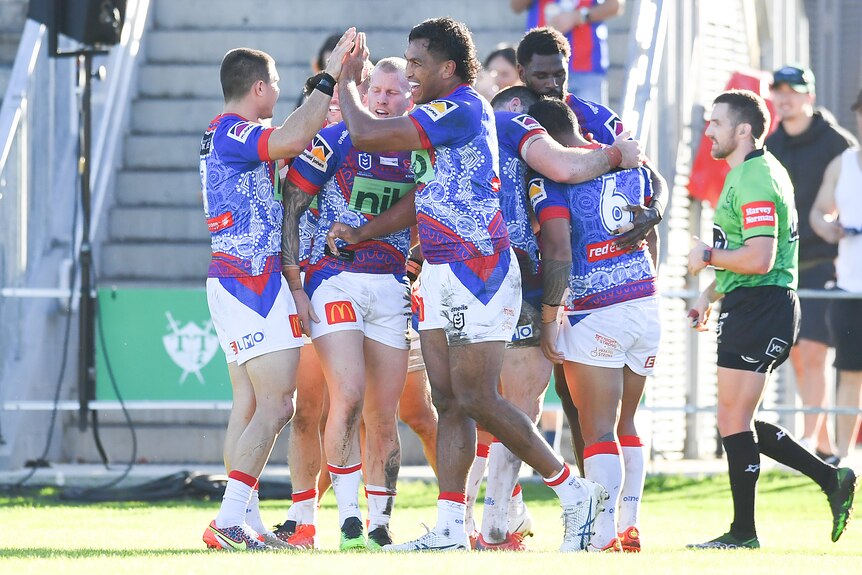 Newcastle Knights players high-five and hug after a try in an NRL game against the Warriors.