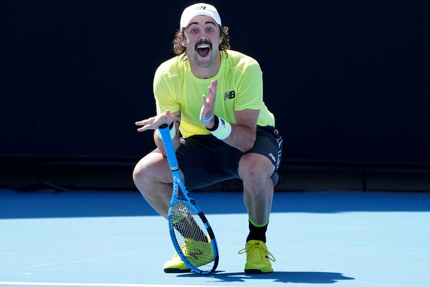 A male tennis player leans on his racquet as he makes a facial expression at the Australian Open.