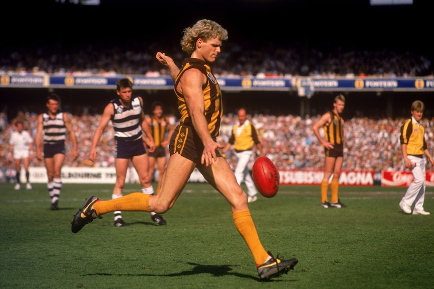 Dermott Brereton with a curly blond mullet prepares to kick for a goal.