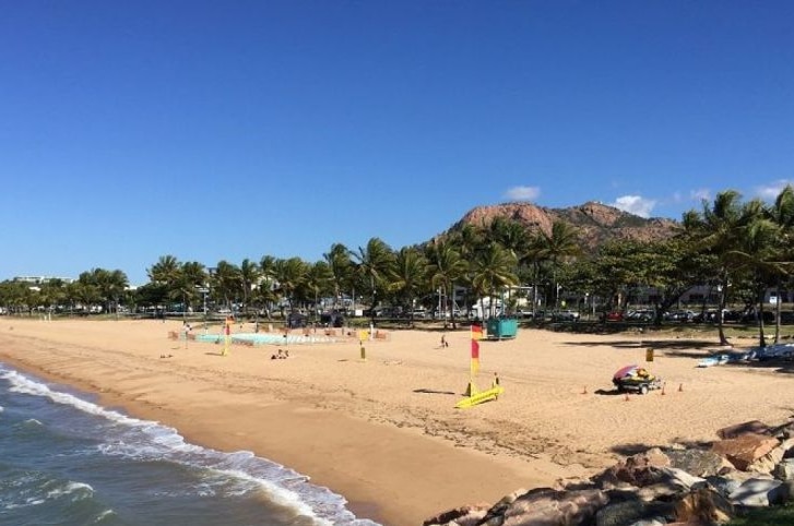 Sand and water at a beach framed by palm trees and Castle Hill in Townsville.