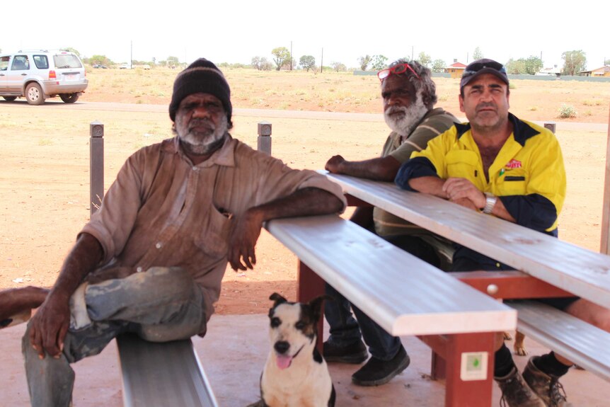 Three men sitting at a public bench with a dog