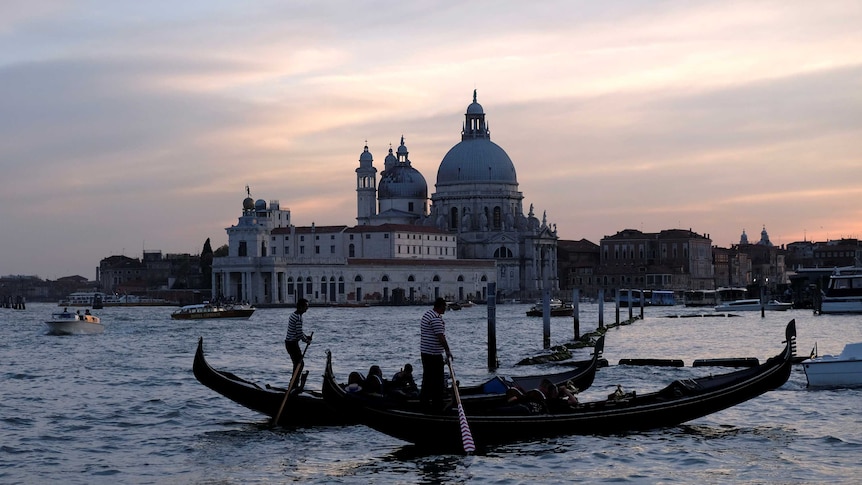 Gondoliers row as tourists enjoy a ride along a canal.