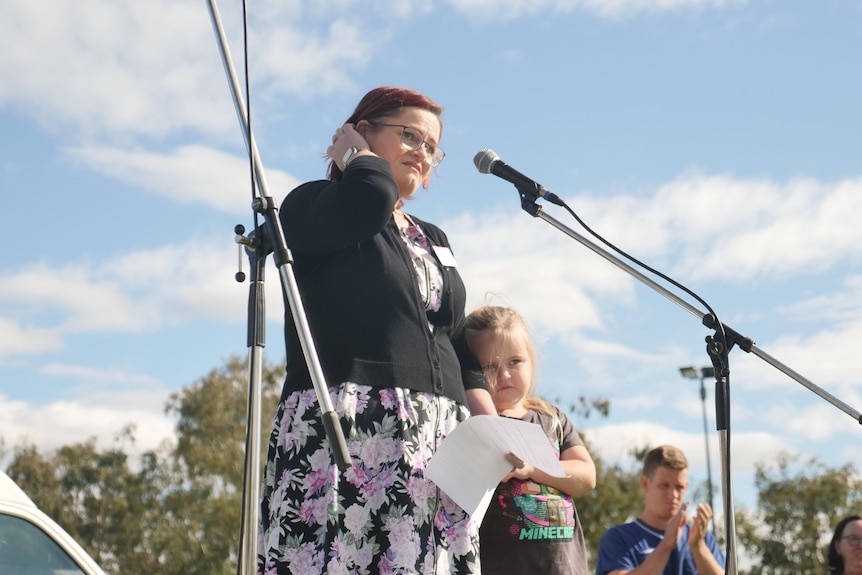 A woman stand besides a child on stage behind a microphone