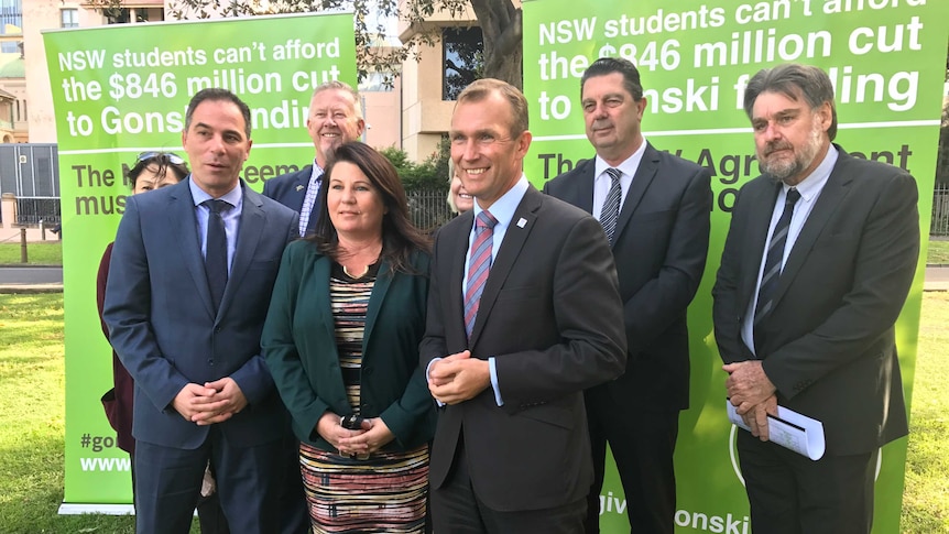 A group, including NSW MPs, stand in front of two sings advocating for education spending.