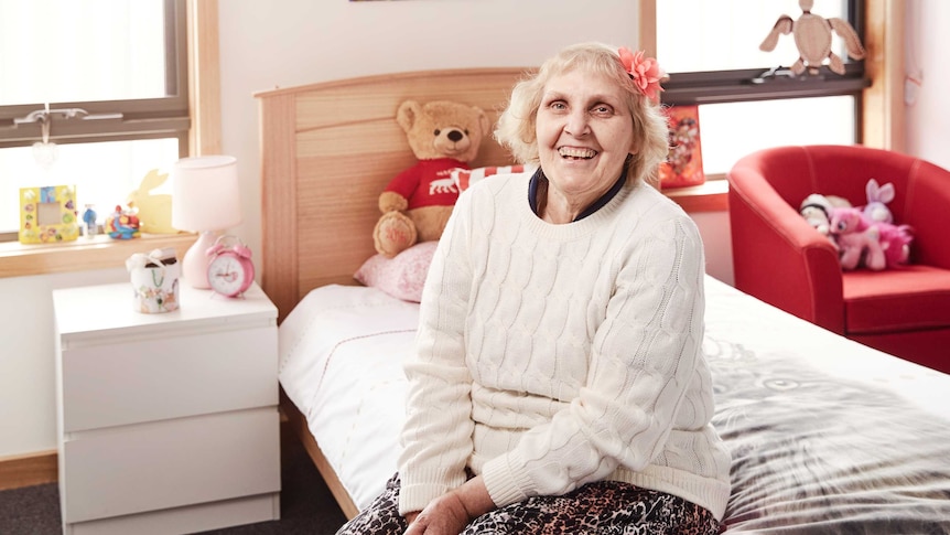 A smiling woman sits on a bed.