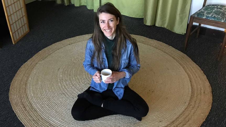 Massage therapist and yoga instructor Sally Kluss sitting on a mat with a cup of tea.